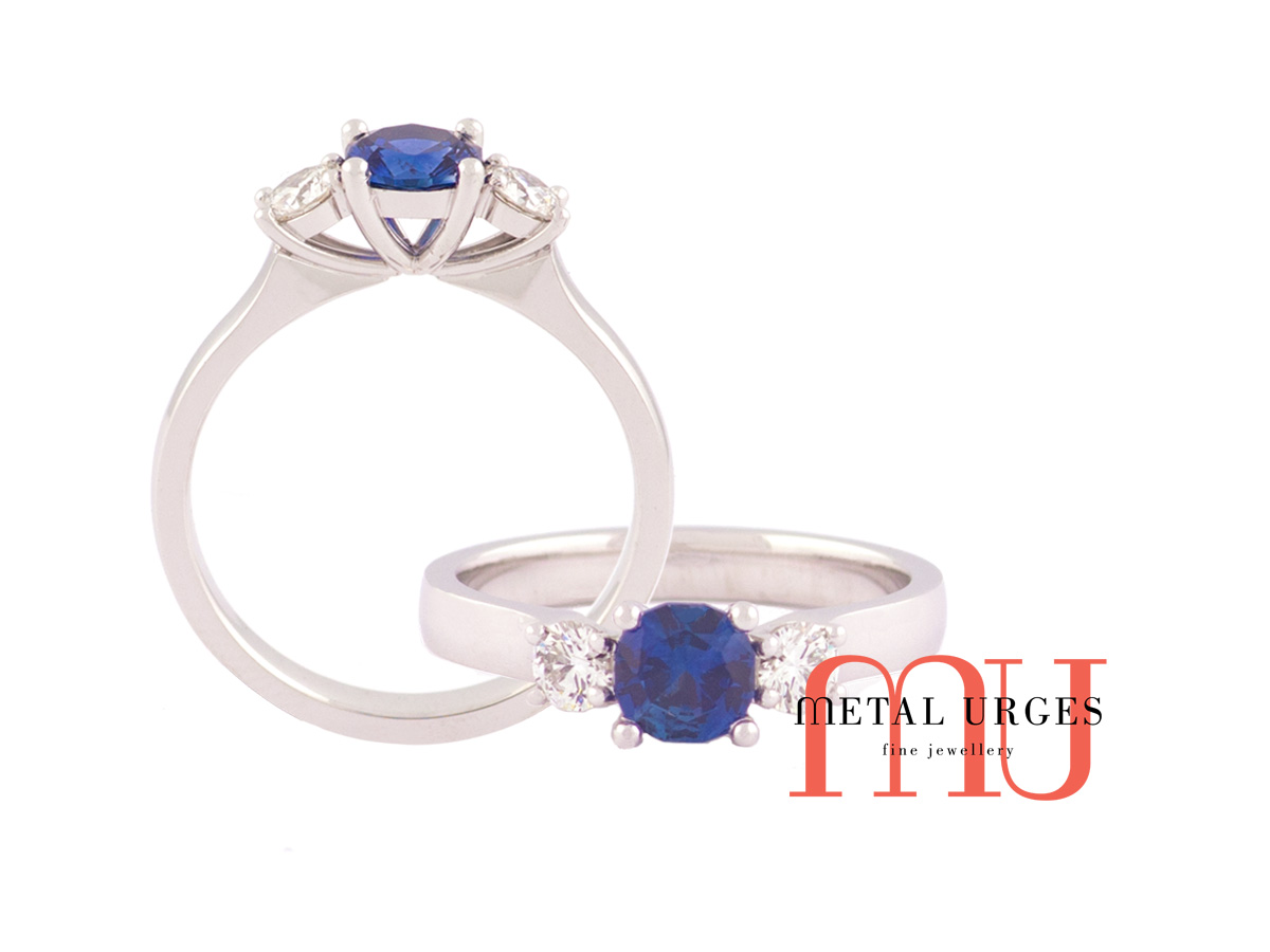 Blue natural sapphire, cushion cut, flanked by white diamond set as a 3 solitaire engagement rings