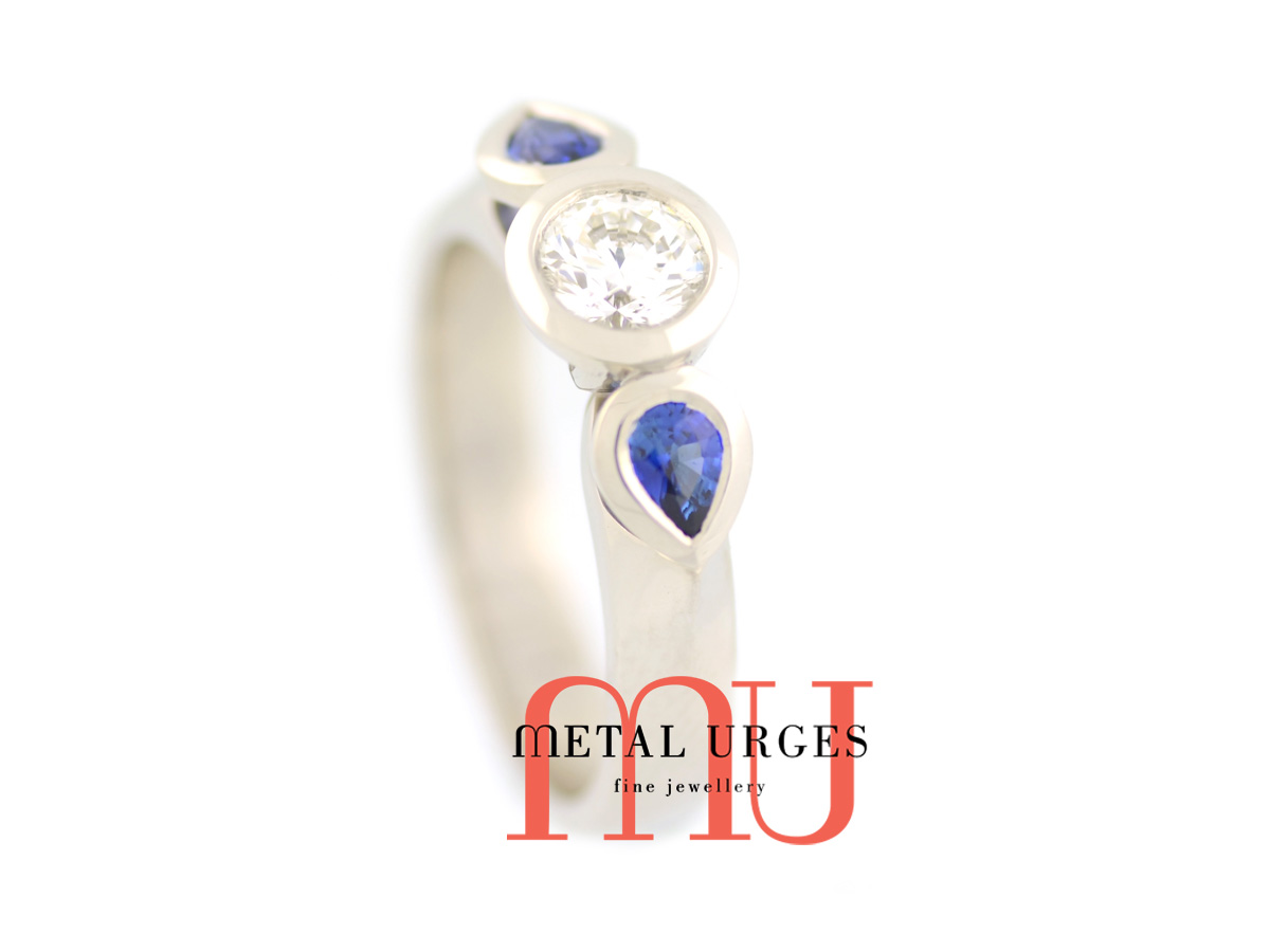 18ct white gold bezel set, natural round white diamond with two tear drop bezel set blue Sri Lankan sapphires either side. Custom made in Australia.